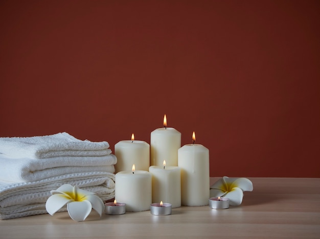 Composição de spa com velas aromáticas acesas e flores de plumeria na mesa de madeira