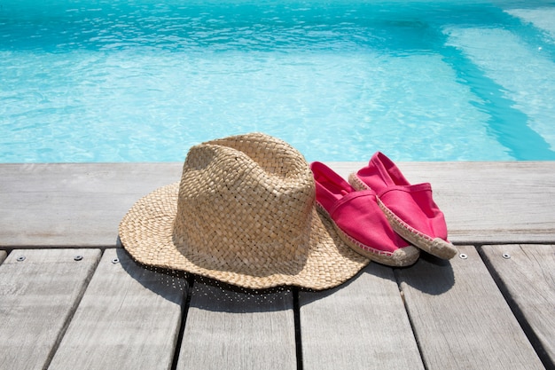 Composição de verão com sapatos de chapéu no deck de madeira e piscina