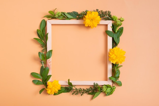 Composição de verão ou primavera em um fundo laranja flores e folhas com vista superior do espaço de cópia de moldura de madeira quadrada conceito floral de primavera de verão