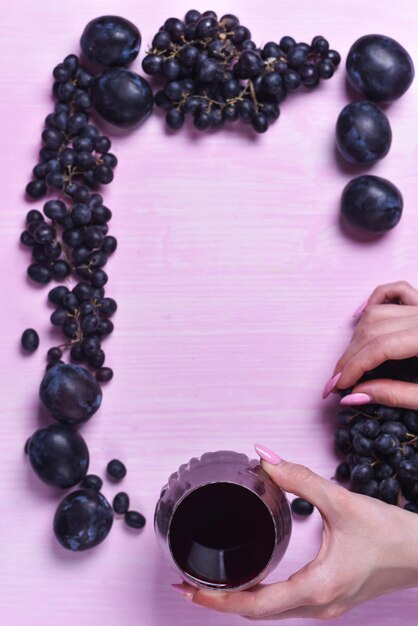 Composição de vinho, uva e ameixa em um fundo rosa