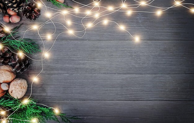 Composição decorativa de natal e ano novo. vista superior, plano de fundo com espaço de cópia para o seu texto. guirlandas, cones, nozes, avelãs, galhos de thuja em uma mesa de madeira.