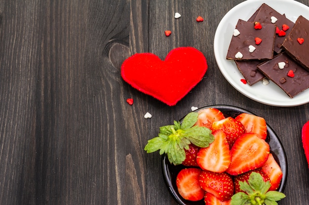 Composição do dia dos namorados com chocolate, morangos maduros frescos e corações vermelhos de têxteis