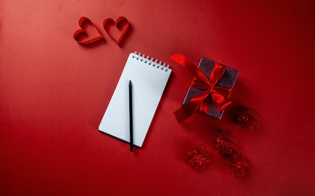 Composição do dia dos namorados com papel de nota em branco com caneta e caixa de presente em fundo vermelho