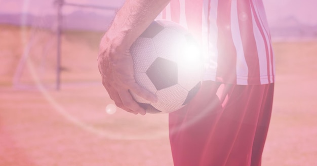 Composição do jogador de futebol segurando uma bola no campo de futebol com luz brilhante