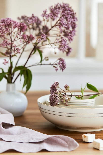 Composição elegante de design de interiores de sala de jantar elegante com mesa rústica, porcelana bonita, flores e acessórios de cozinha. Beleza nos detalhes. Modelo.