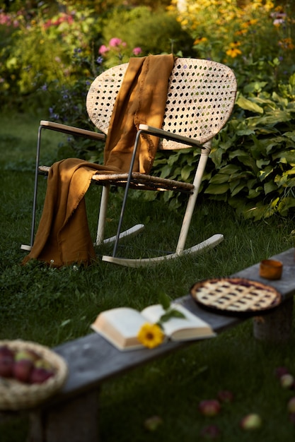 Composição elegante de jardim rural com poltrona de vime de design, banco de madeira, xadrez, alimentos, bebidas e acessórios elegantes. muitas flores coloridas. clima de verão.