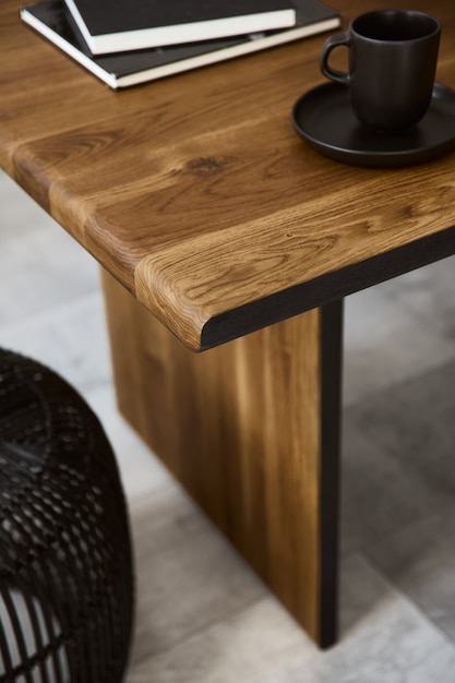 Composição elegante de mesa de madeira artesanal com design pufe de rattan preto, caneca, livro e piso de concreto. Modelo.