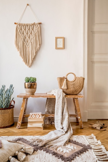 Composição elegante do interior da sala de estar com moldura simulada, banco de madeira, travesseiro, xadrez, bolsa de mulher, livros, cactos, macramê, planta, decortaion e acessórios pessoais elegantes na decoração moderna.