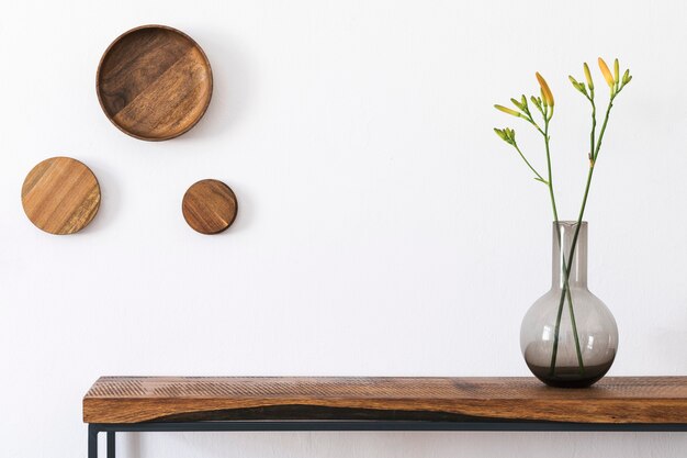 Composição elegante do interior da sala de estar com parede branca, plantas verdes em vasos de design moderno branco no console escandinavo de madeira. Conceito minimalista. Copie o espaço.