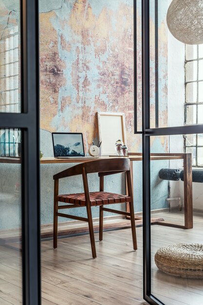 Composição elegante e moderna do interior do espaço de trabalho criativo com mesa e cadeira de madeira, planta e acessórios. quarto espaçoso com paredes criativas e piso em parquet.