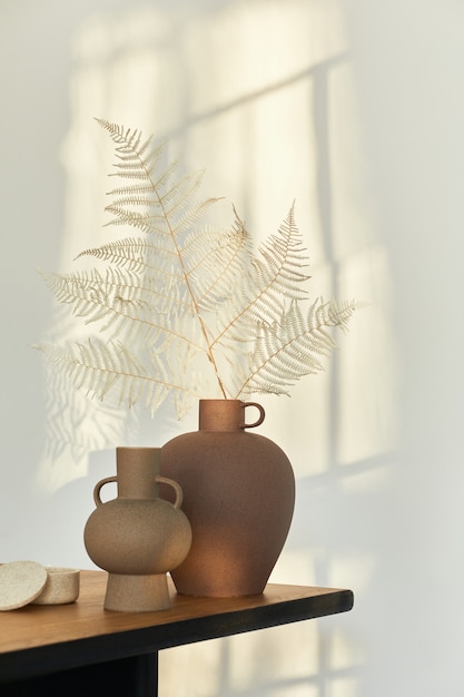 Foto composição elegante na mesa de madeira com vasos de design com flores secas. lindas sombras na parede. conceito abstrato no interior moderno.