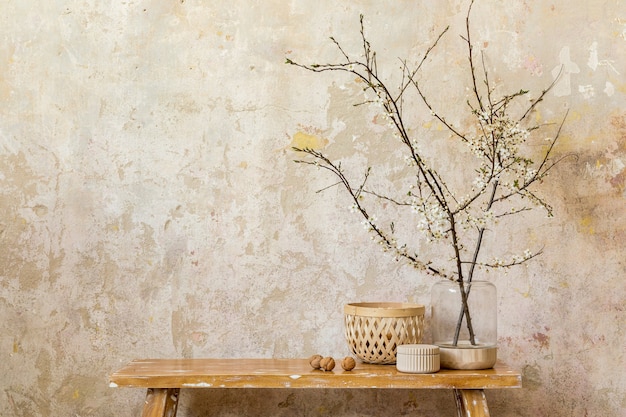 Composição elegante no interior da sala de estar com banco de madeira de design, flores secas em um vaso, parede grunge, caixas e acessórios pessoais elegantes na decoração moderna da casa. Copie o espaço.