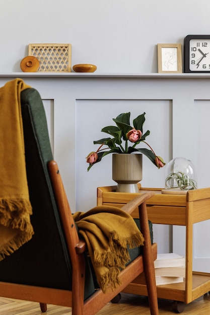 Foto composição elegante no interior da sala de estar com poltrona de design, xadrez, relógio, planta, planta de ar, livro, painéis de madeira com prateleira e acessórios pessoais elegantes em decoração moderna.