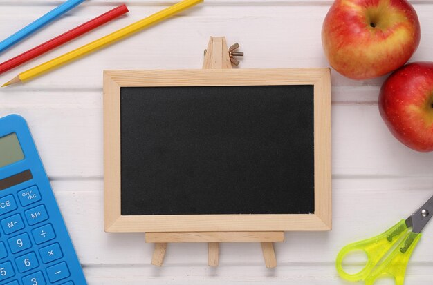 Composição escolar de material escolar e mini lousa em branco na mesa de madeira branca