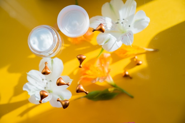 Composição flatlay com flores creme sobre fundo amarelo - conceito de cosmético de vitaminas naturais ...