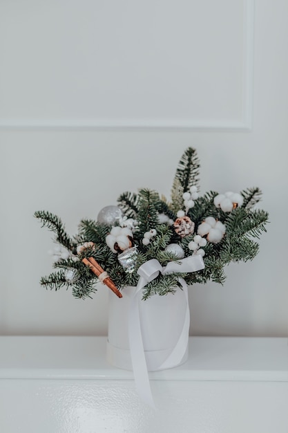 Composição floral de Natal em uma caixa de chapéu branco com galhos de pinheiro, algodão, paus de canela e bolas de Natal. O conceito de um Ano Novo e Natal elegantes