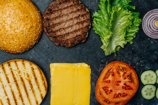 Composição home feita do hamburguer (receita). produtos para o hambúrguer clássico sobre um fundo escuro.