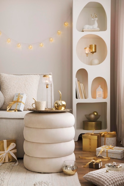 Composição incrível na prateleira de design branco com luzes de decoração de natal presentes lanternas velas de veado estrelas sofá de veludo branco e pufe Papai Noel está chegando Decoração de casa Modelo