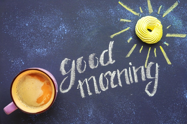 Composição matinal de café e rosquinha como um sol na inscrição do quadro-negro bom dia escrito com giz