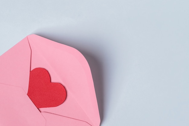 Composição mínima com um envelope rosa com um coração vermelho dentro para o dia dos namorados