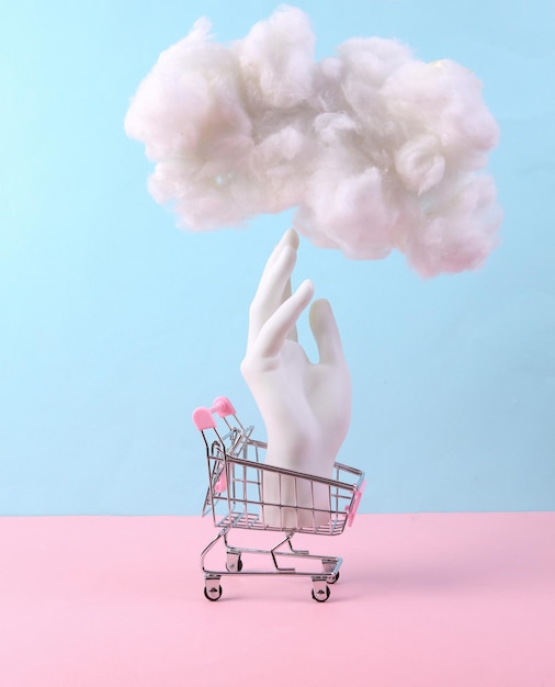 Composição minimalista com mão no carrinho de compras e nuvem fofa em um fundo azul pastel rosa Minimalismo Concept art