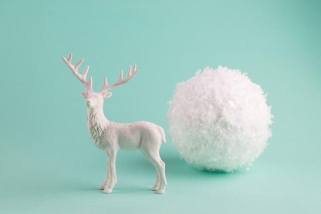 Composição minimalista de inverno com veado branco e uma grande bola de neve decorativa.