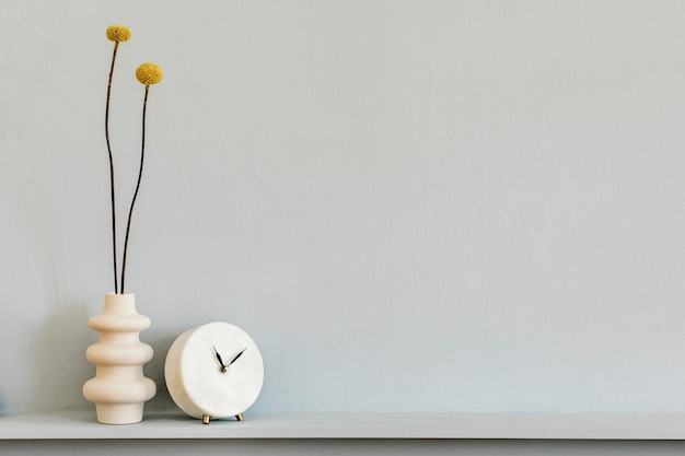 Composição minimalista na prateleira com flores secas em vaso de design e relógio branco. Parede cinza. Copie o espaço.