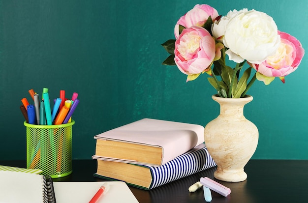 Composição na mesa com livros e flores sobre fundo verde quadro-negro