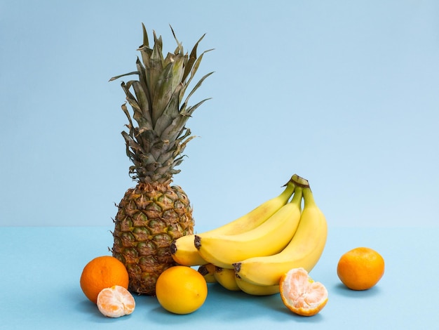Composição natural de frutas tropicais. Abacaxi fresco, banana, limão e tangerinas sobre fundo azul.
