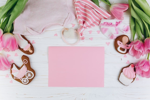 Foto composição para recém nascidos em um fundo de madeira com roupas, tulipas cor-de-rosa e um biscoito