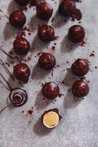 Composição plana com trufas de chocolate em papel manteiga e uma bala de chocolate cortada ao meio e recheada com caramelo salgado. Ferramenta de chocolate ao lado de doces