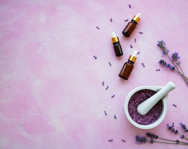 Composição plana leiga com flores de lavanda e cosméticos naturais em fundo rosa