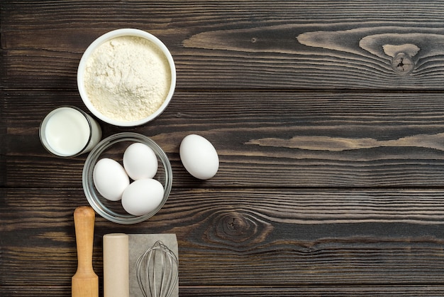 Composição plana leiga com ingredientes para fazer massa em um fundo escuro de madeira com espaço de cópia.