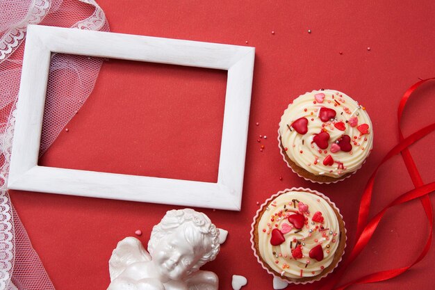 Composição plana para cumprimentos de dia dos namorados. Cupcakes, anjo, moldura em um fundo vermelho. Copie o espaço para o seu texto