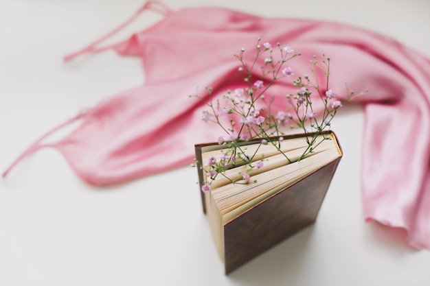 Composição romântica com um livro com flores dentro e vista superior de tecido de seda rosa simulada