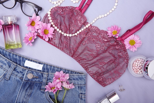 Composición con accesorios de ropa femenina de moda y flores sobre fondo lila