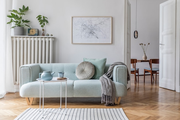 Composición acogedora y creativa del elegante diseño de interiores de la sala de estar con sofá verde, muebles de madera, plantas y accesorios. Paredes blancas, suelo de parquet.