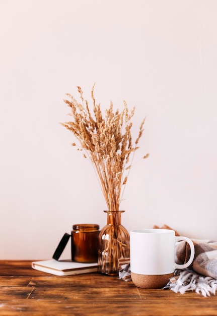 Composición acogedora de otoño. Una taza de café, una manta, una vela, flores secas sobre un fondo claro.