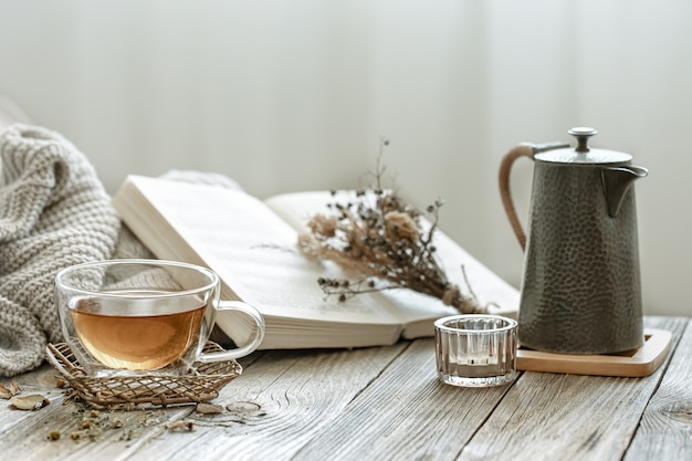 Composición acogedora con una taza de té y un libro en el interior de la habitación sobre un fondo borroso.