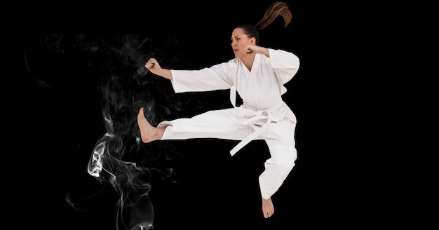Composición del artista de karate marcial femenino con cinturón blanco en el aire sobre humo y espacio de copia