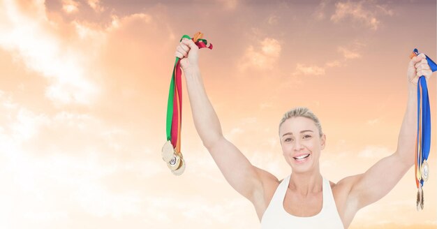 Composición de la atleta femenina caucásica sonriente fuerte sosteniendo medallas sobre el cielo