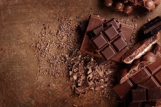 Composición de barras y trozos de diferente leche y chocolate negro, cacao rallado sobre un fondo marrón vista superior de cerca