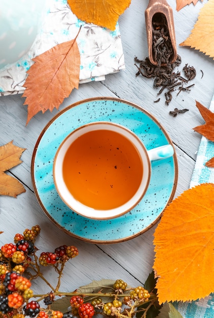 Composición bodegón de una taza con té de hojas calientes con bayas y hojas de otoño sobre una superficie de madera