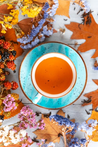 Composición bodegón de una taza con té de hojas calientes con bayas y hojas de otoño sobre una superficie de madera