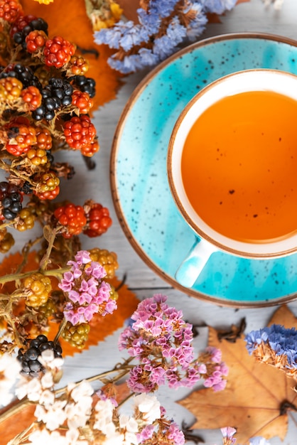 Composición bodegón de una taza con té de hojas calientes con bayas y hojas de otoño sobre una superficie de madera