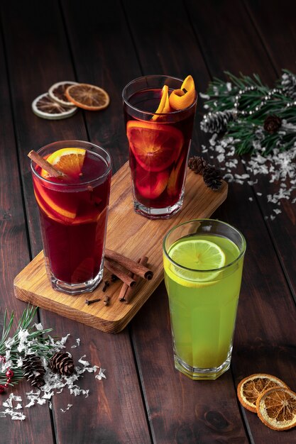 Composición de bodegón con tres vasos de bebida refrescante de invierno rojo y verde o vino caliente con rodajas de naranja sobre un fondo de madera oscura con nieve