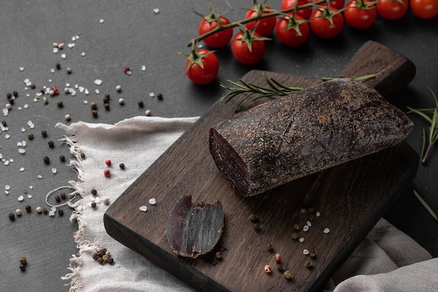 Composición de bodegón con un trozo de jamón seco ahumado rojo de carne de alce sobre una tabla de cortar de madera, vista lateral