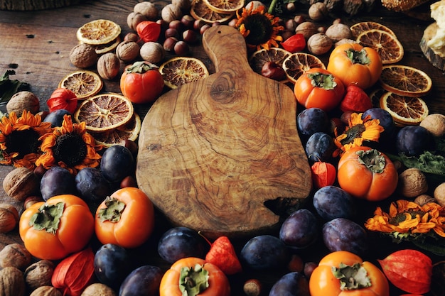 Composición de bodegones otoñales con frutas y verduras frescas Surtido de ciruelas caqui nuez girasoles y naranjas secas y tablero de madera rústico espacio de enfoque selectivo para texto