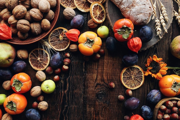 Composición de bodegones de otoño con frutas y verduras frescas Surtido de ciruelas caqui manzanas nuez girasoles y naranjas secas en la mesa de madera rústica vista superior espacio de copia