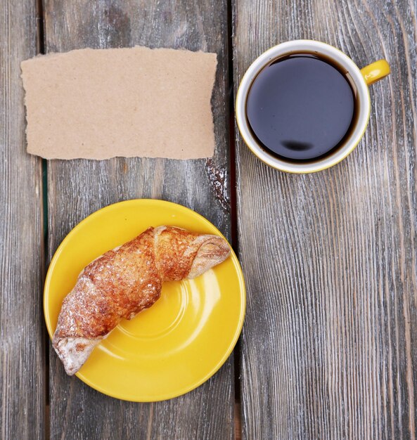 Composición de café croissant recién hecho y tarjeta de papel sobre fondo de madera